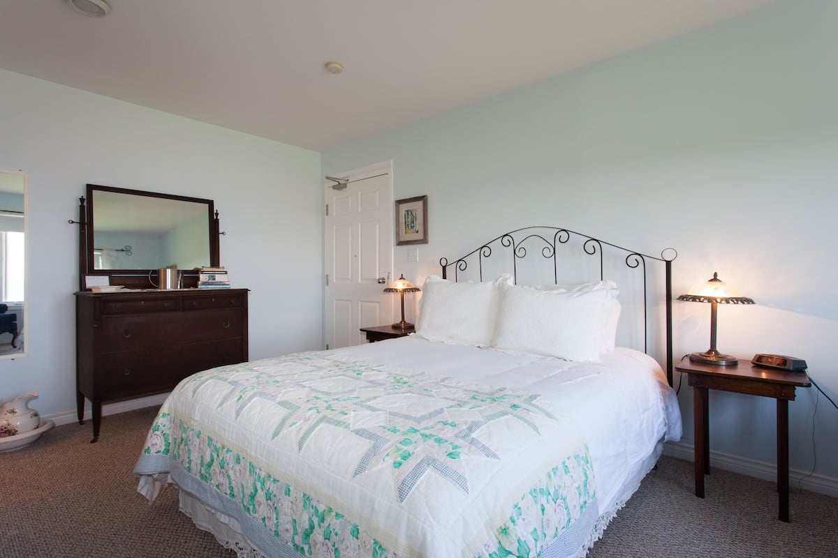A bedroom with a bed, dresser, bedside tables, and a mirror.