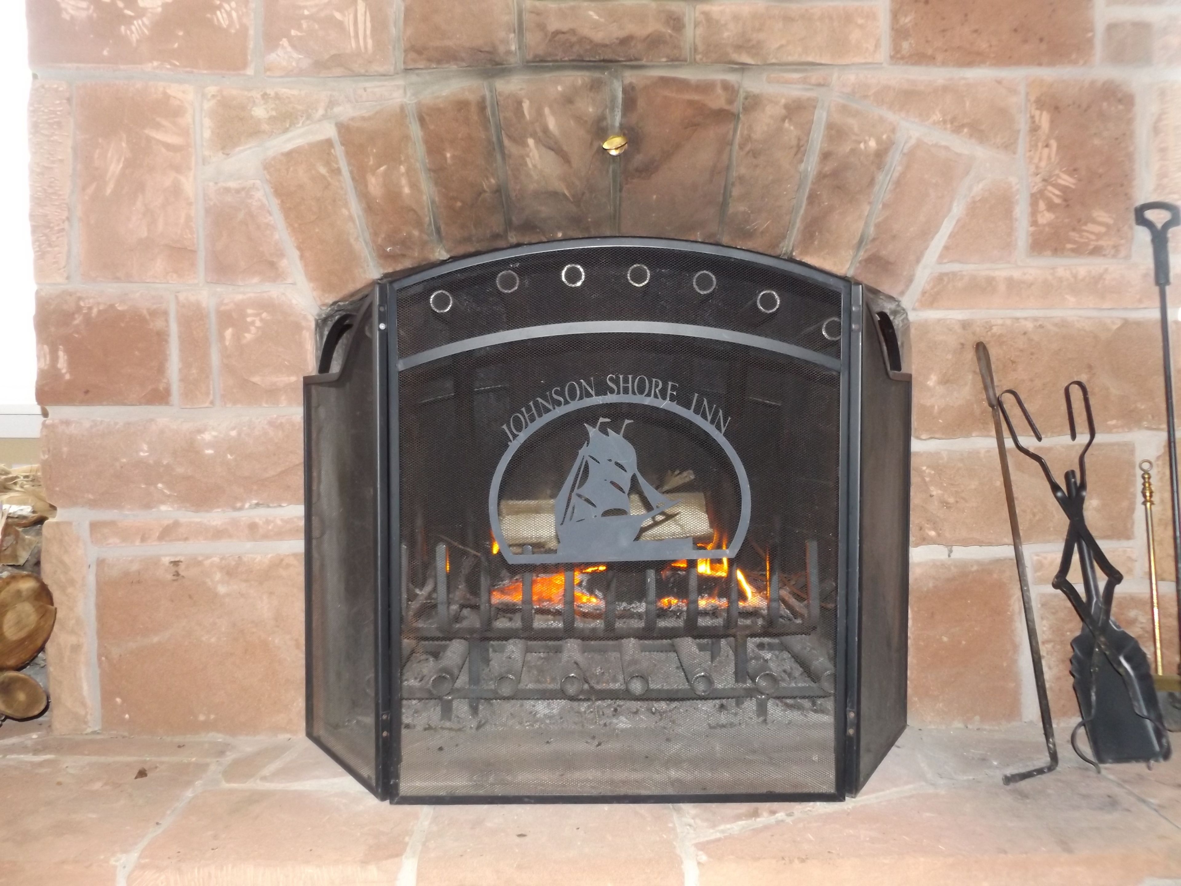 A fireplace with a metal screen, a logo, and a fire burning inside.