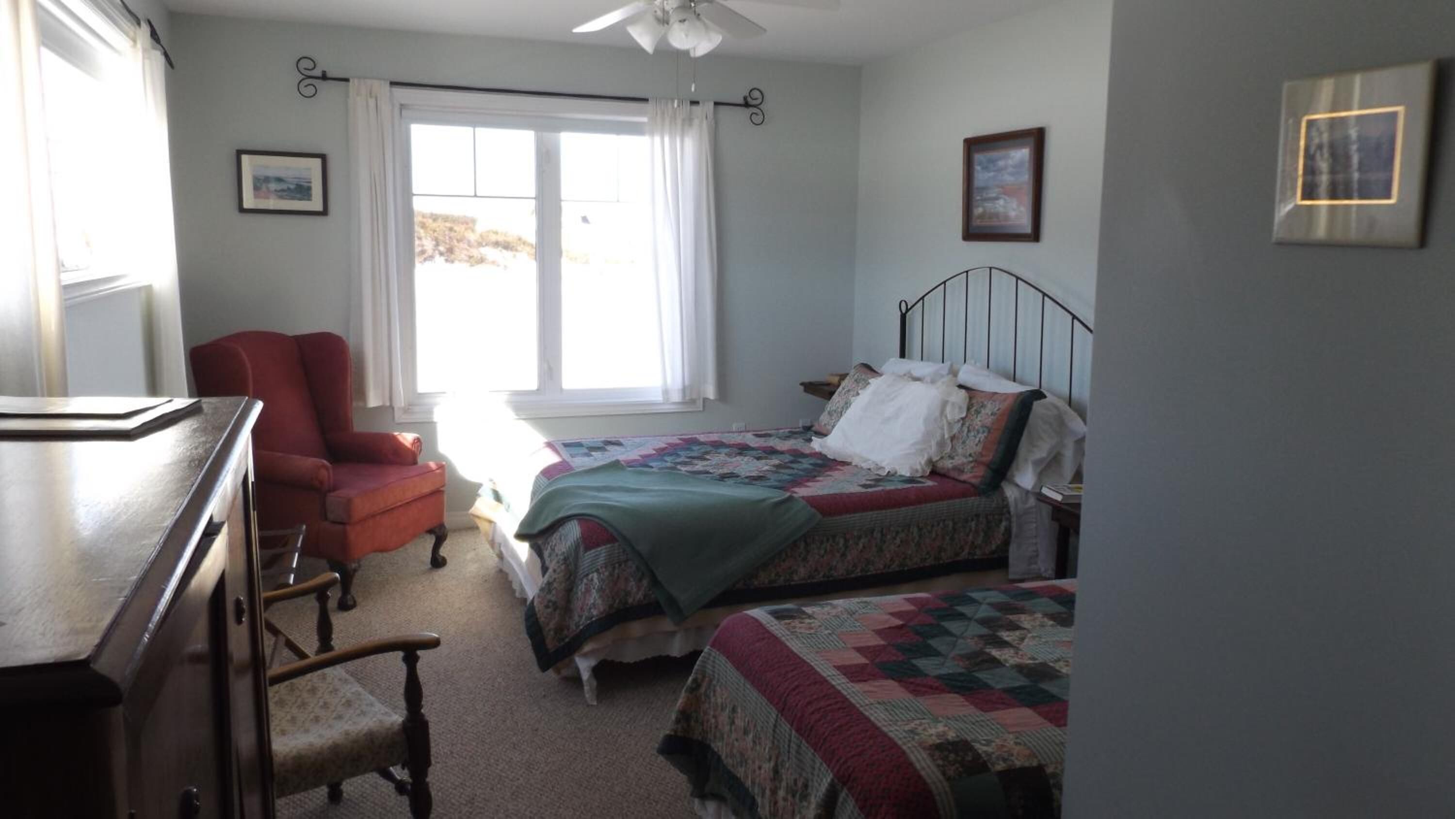 A bedroom with two beds, a desk, a chair, and a window with curtains.
