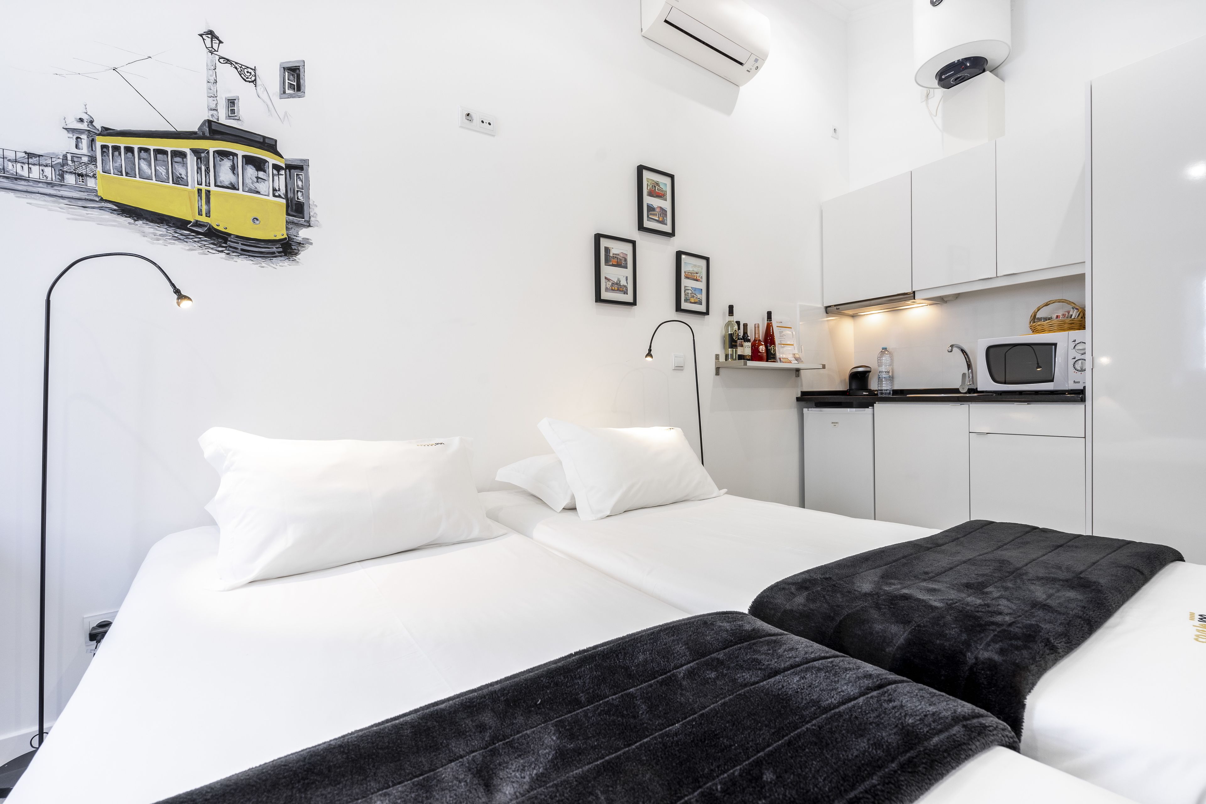 Una camera d'hotel moderna con un letto, un divano nero, un angolo cottura e un'opera d'arte a parete raffigurante un tram.