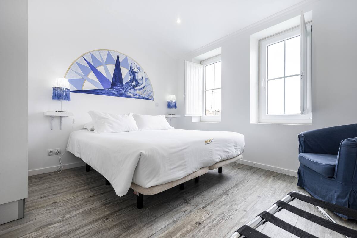 Un dormitorio moderno con una cama, una silla azul y un ventanal grande.