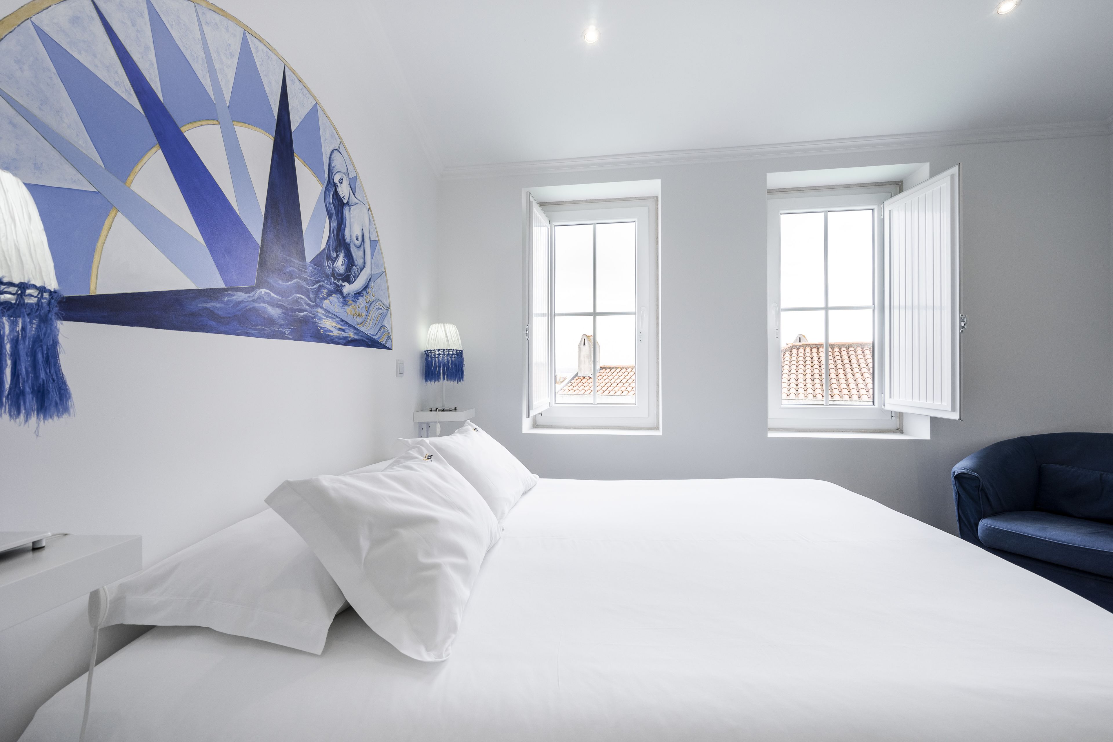 A bedroom with a large bed, two windows, a painting, and a blue chair.