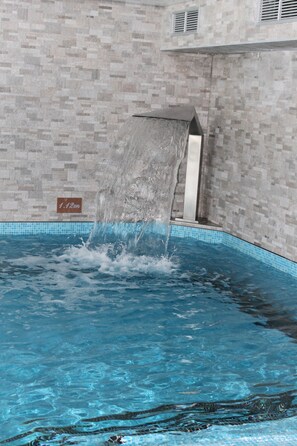 Piscina con caída de agua, paredes enlosadas y indicador de profundidad.
