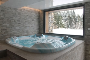 Un jacuzzi con pared de piedra y ventana con vista a un paisaje nevado.