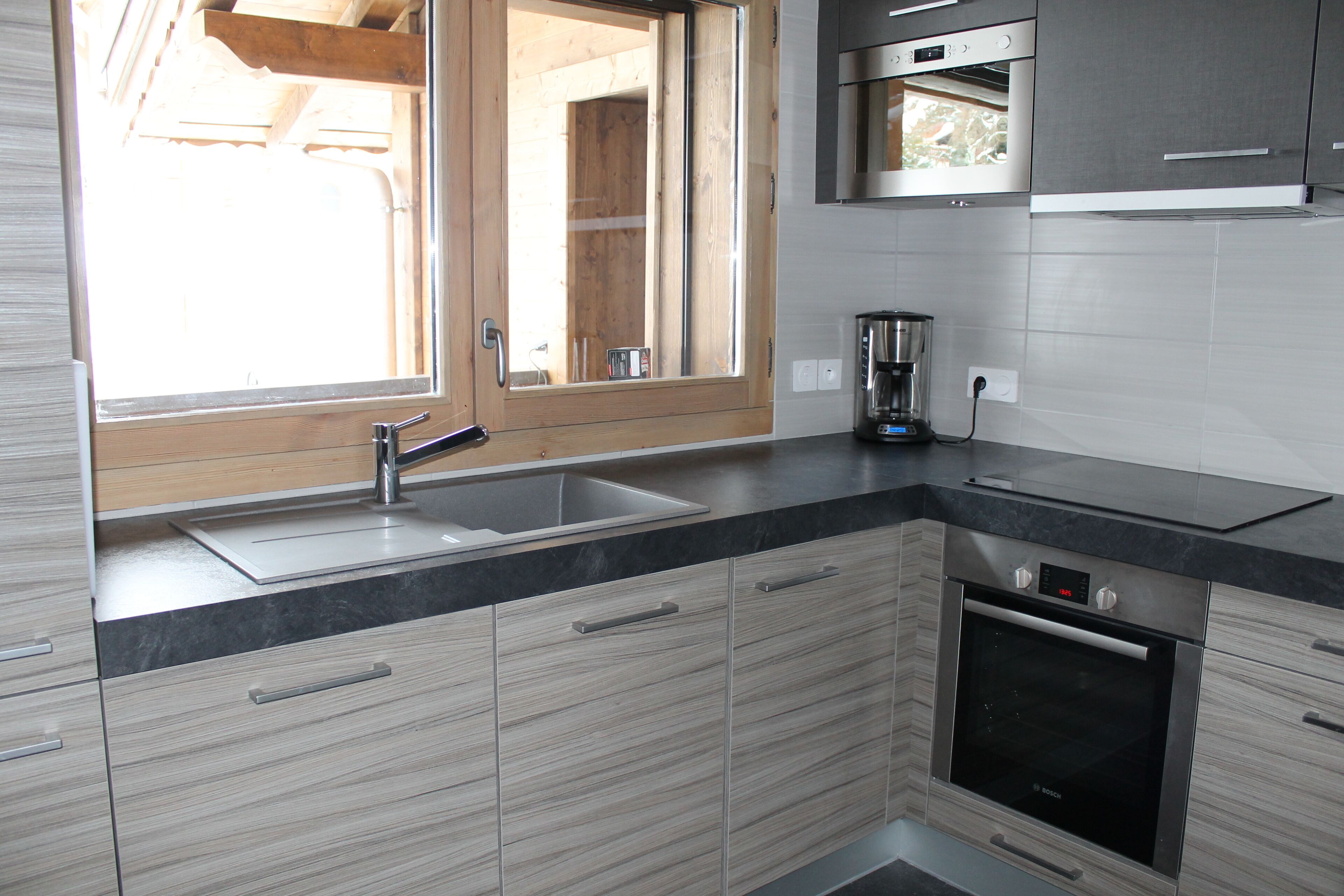 A modern kitchen with a built-in oven, a sink, and a window.