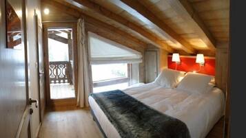 A bedroom with a bed, a window with curtains, a door, and a wooden ceiling.
