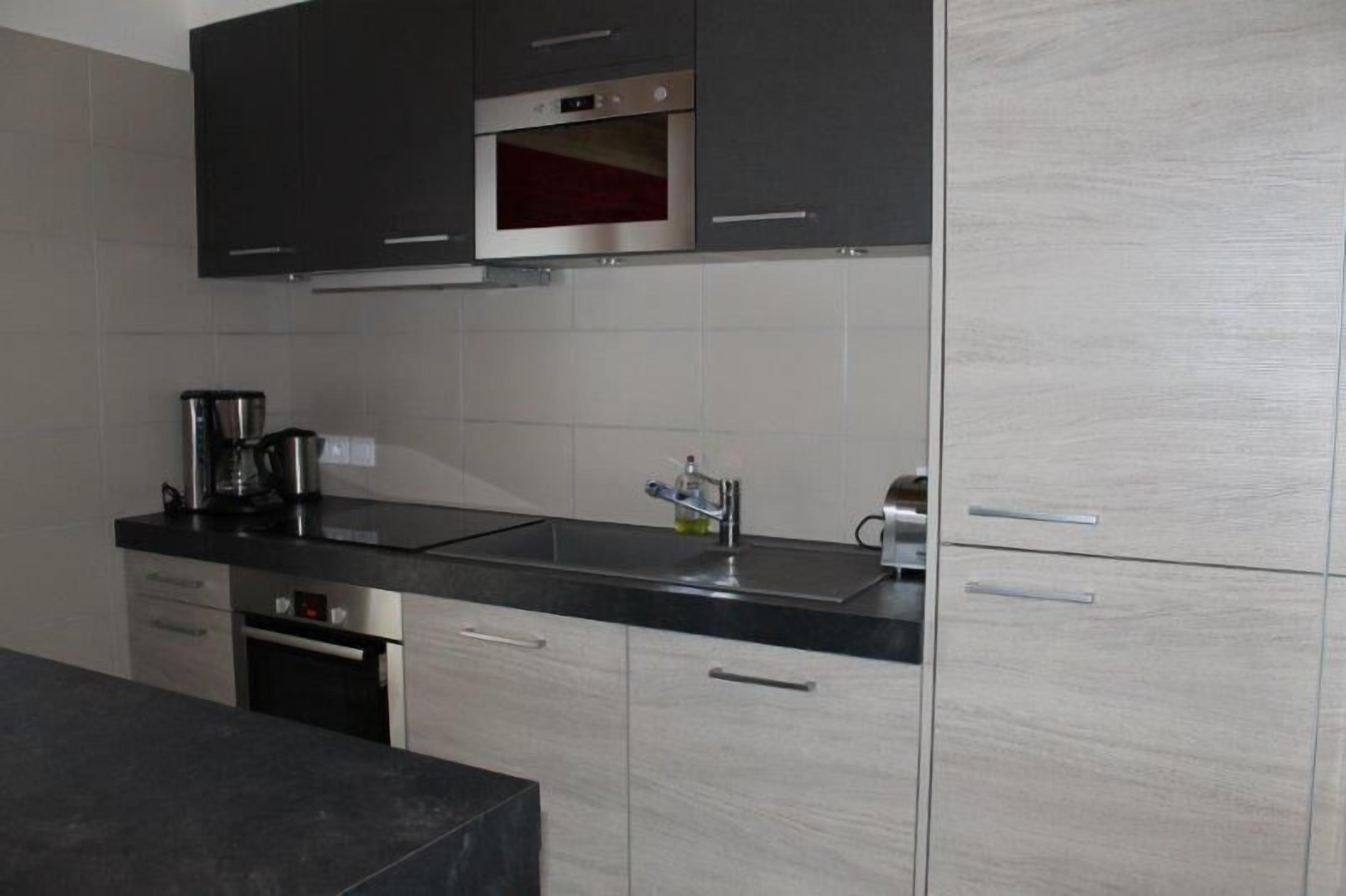 A modern kitchen with stainless steel appliances, a black countertop, and light wood cabinetry.