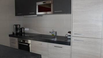 A modern kitchen with stainless steel appliances, a black countertop, and light wood cabinetry.