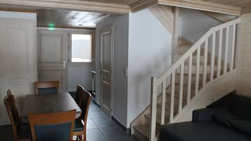 A room with a dining table, chairs, a sofa, and a wooden staircase.