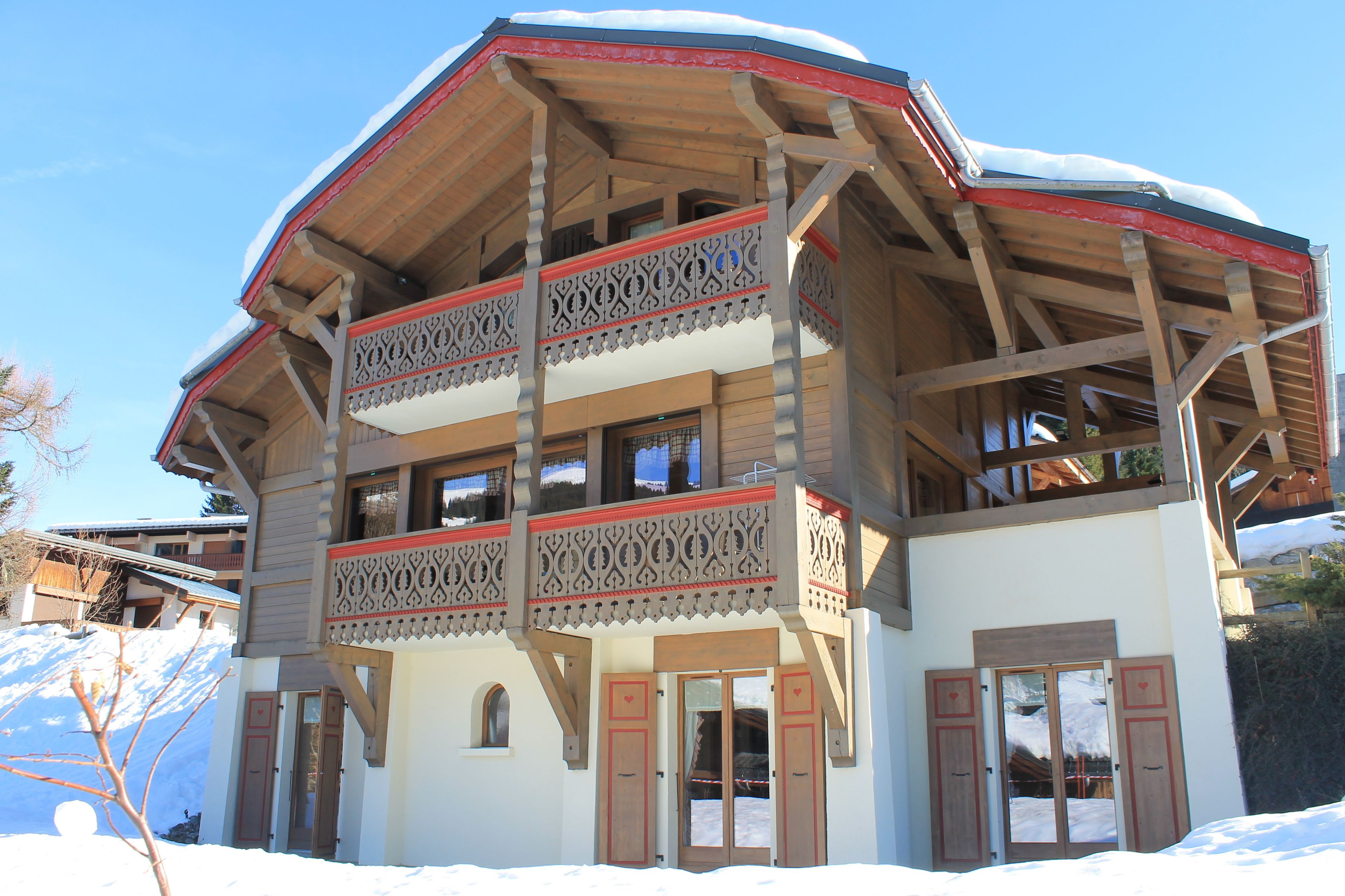A two-story chalet with a wooden exterior, balconies with intricate railings, and a snow-covered roof.