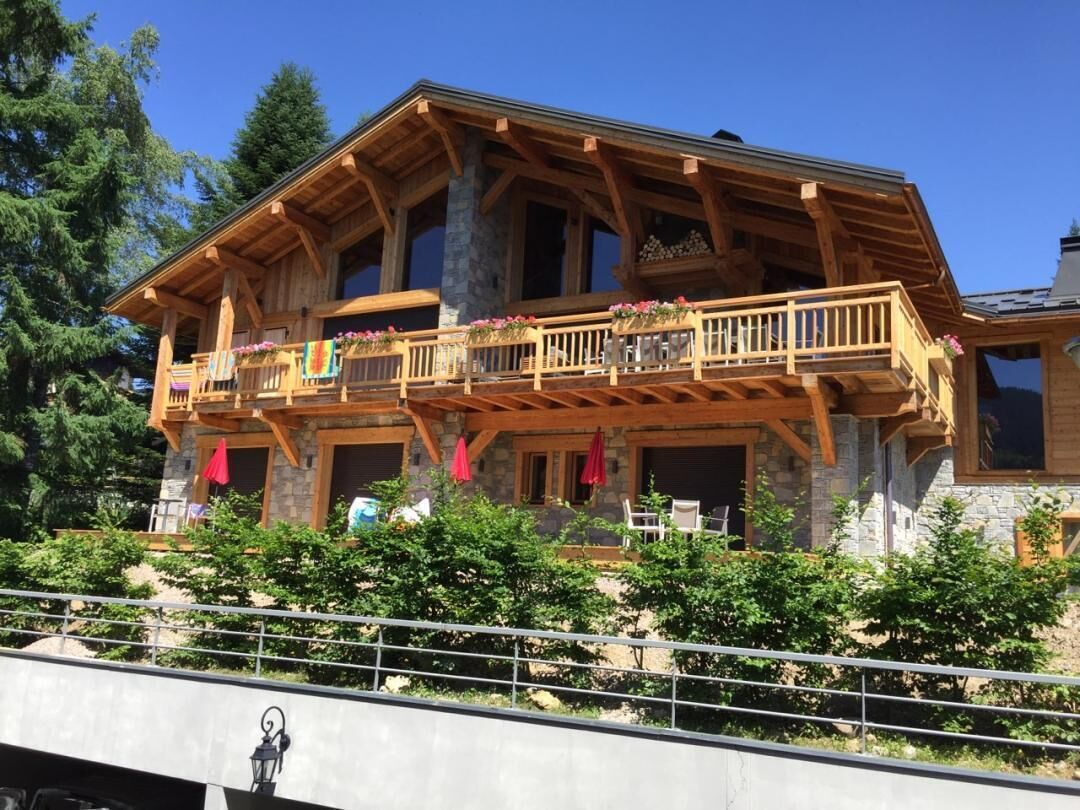 A wooden chalet with a balcony, stone foundation, and outdoor seating area.