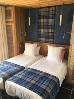 Una habitación con dos camas, paredes de madera, colcha escocesa y una pared de acento azul.