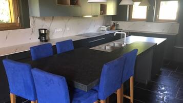 A modern kitchen with a central island, blue bar stools, and pendant lighting.