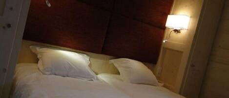 A bed with white linens in a room with wooden paneling and a wall-mounted light fixture.