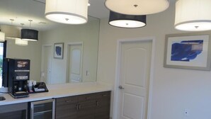 Un baño moderno con un espejo grande, una zona de café y una puerta con un cuadro.