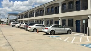 Una fila de coches blancos estacionados en el aparcamiento de un hotel, bajo un cielo azul despejado con nubes.