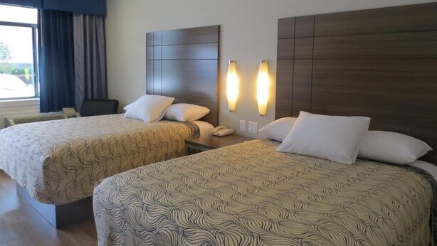 Habitación de hotel con dos camas, un escritorio y una ventana con cortinas.