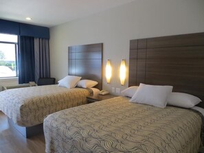 A hotel room with two beds, a desk, and a window with curtains. - Palace Inn Gulfgate (Houston)