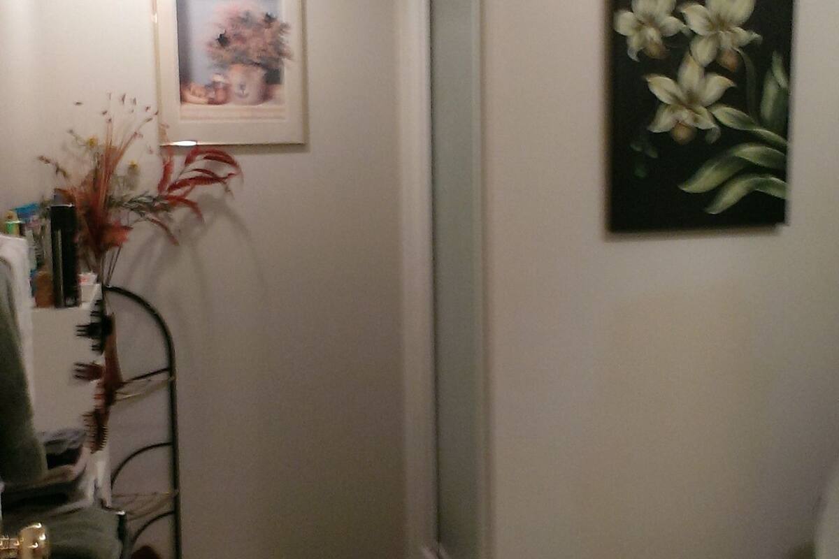 Un baño con inodoro, ducha, lavamanos, espejo, un cuadro enmarco y una planta.