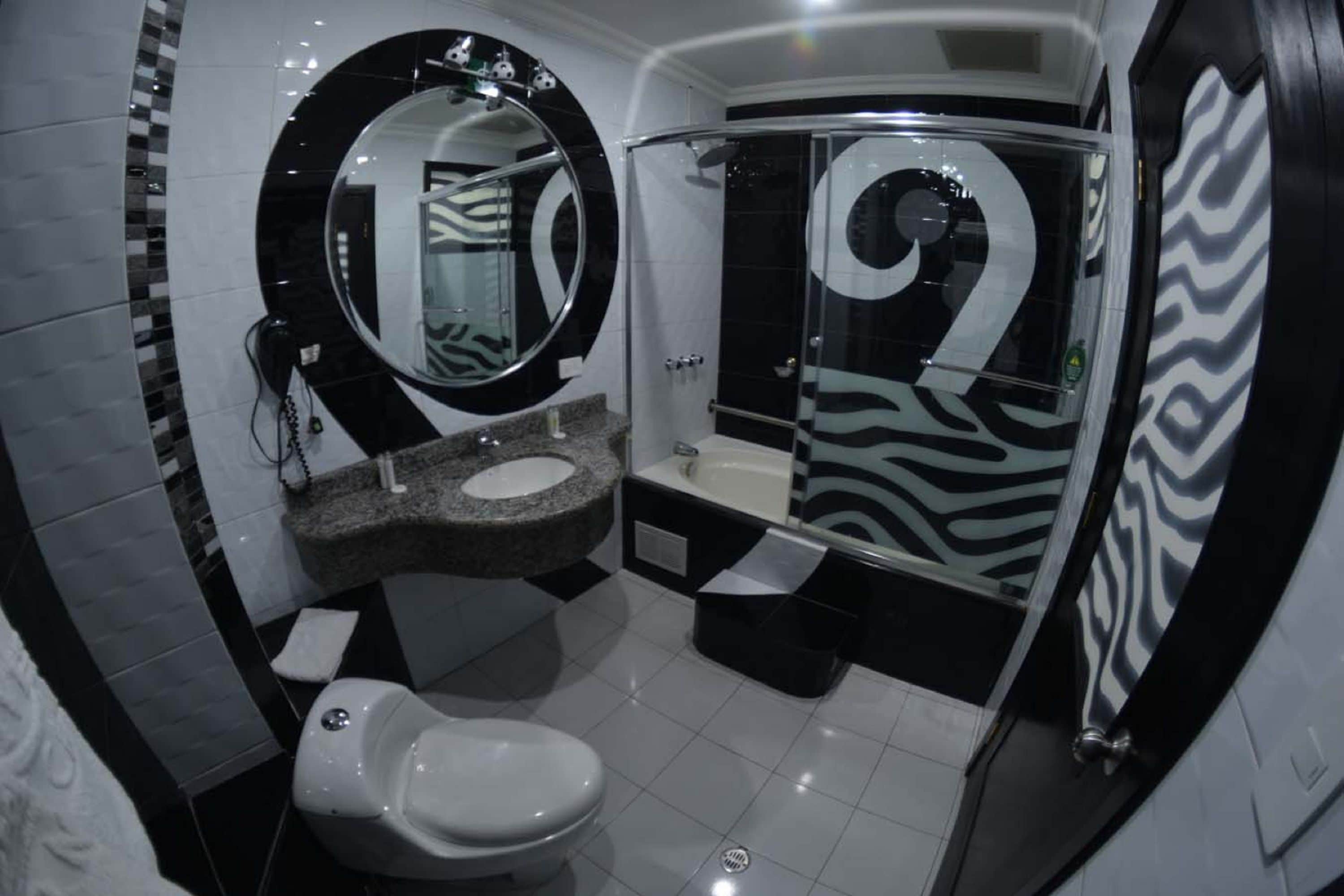 Et moderne badeværelse med et hvidt toilet, en marmorvask, et stort spejl og en brusekabine med zebra-mønster.