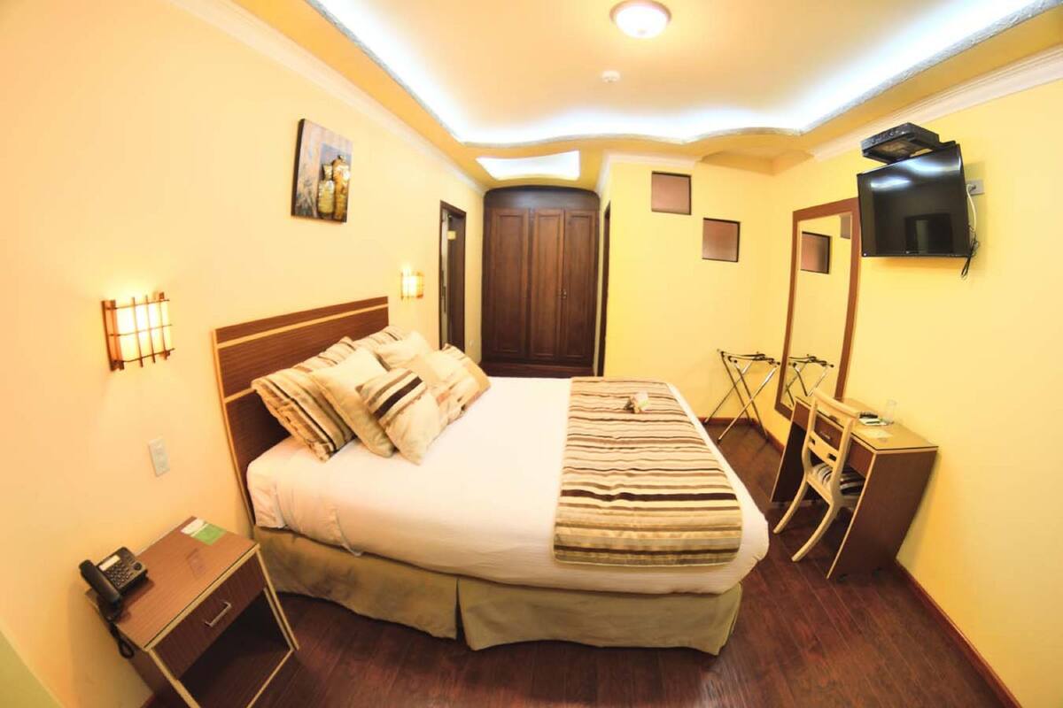 A hotel room with a bed, bedside table, lamp, TV, and a wardrobe.