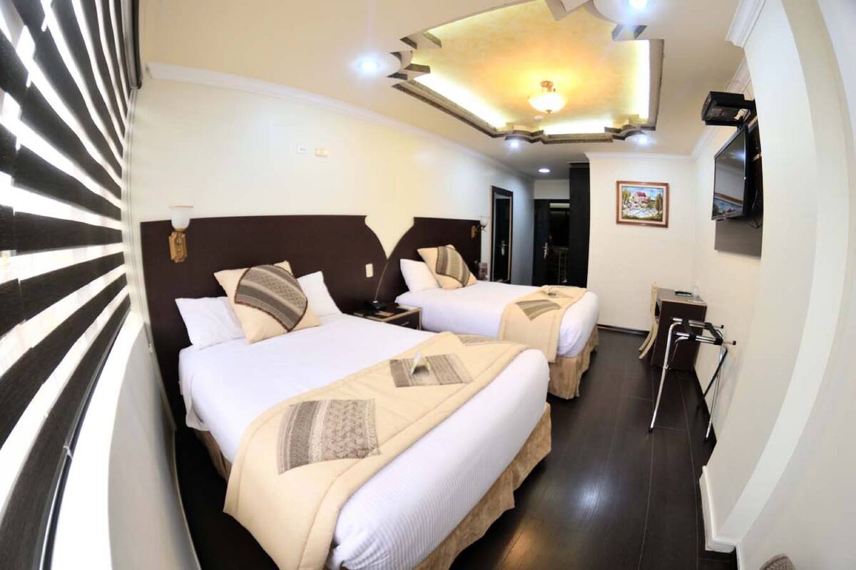 A hotel room with two beds, a ceiling light fixture, a television, and a small table.