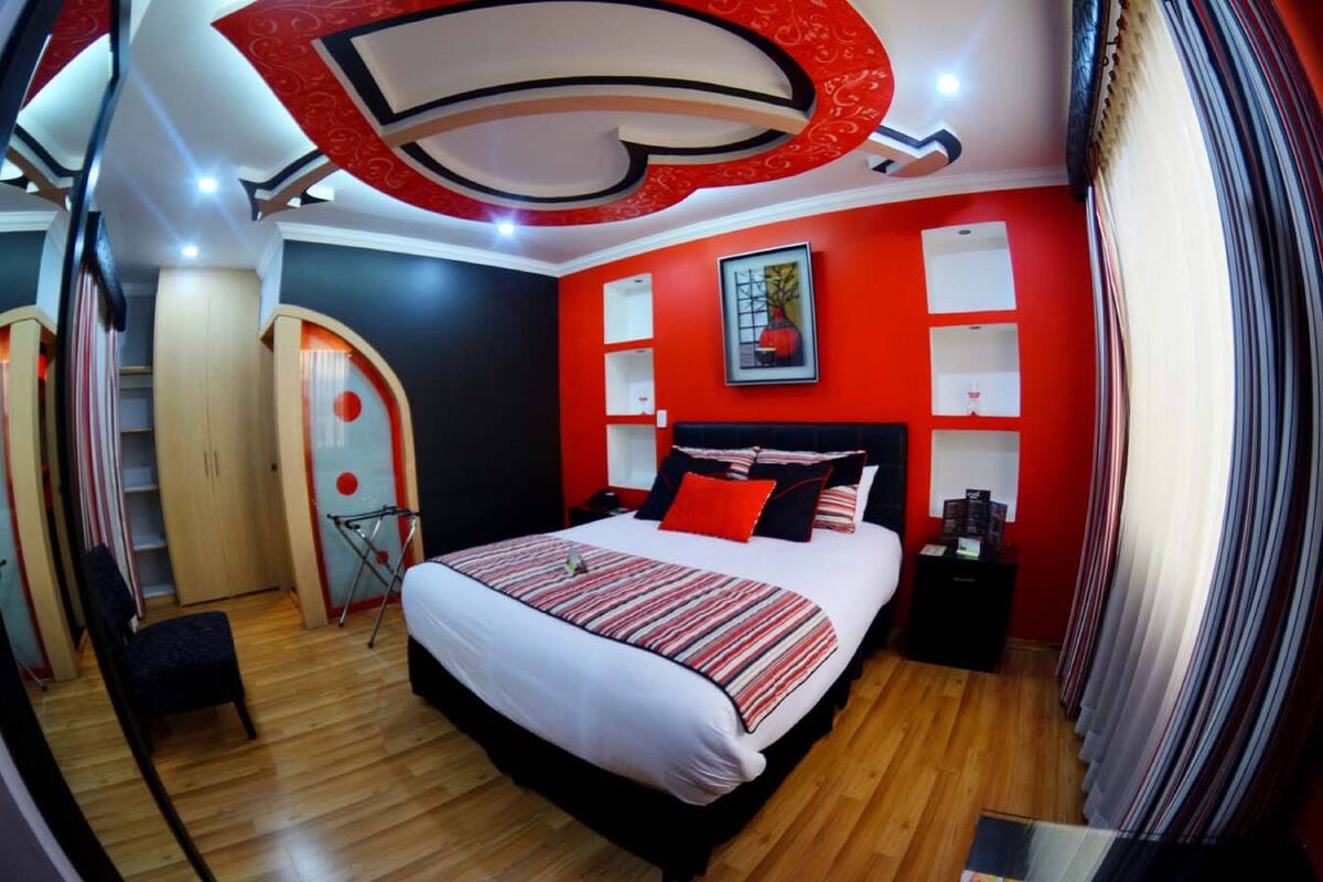 A modern bedroom with a large bed, red walls, and a unique ceiling design.