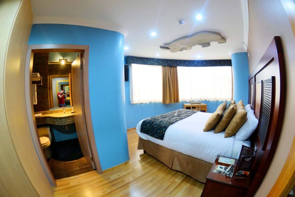 A bedroom with a large bed, a wooden headboard, a small bedside table, and a window with curtains.