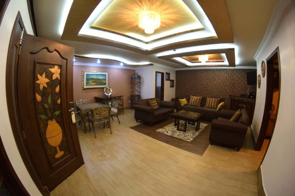 A spacious living room with a dining area, featuring a chandelier, sofas, and a decorative door.