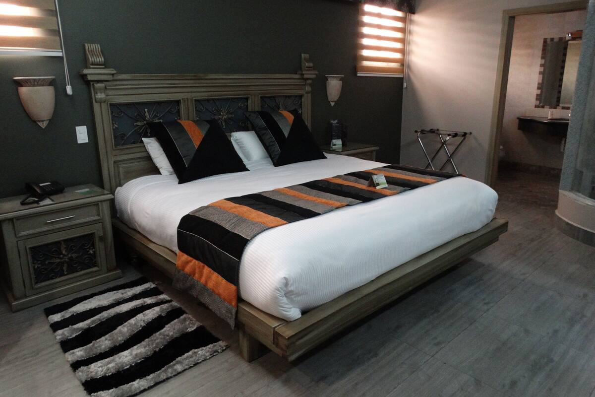 A bedroom with a large bed, bedside tables, a nightstand, a chair, and a mirror.