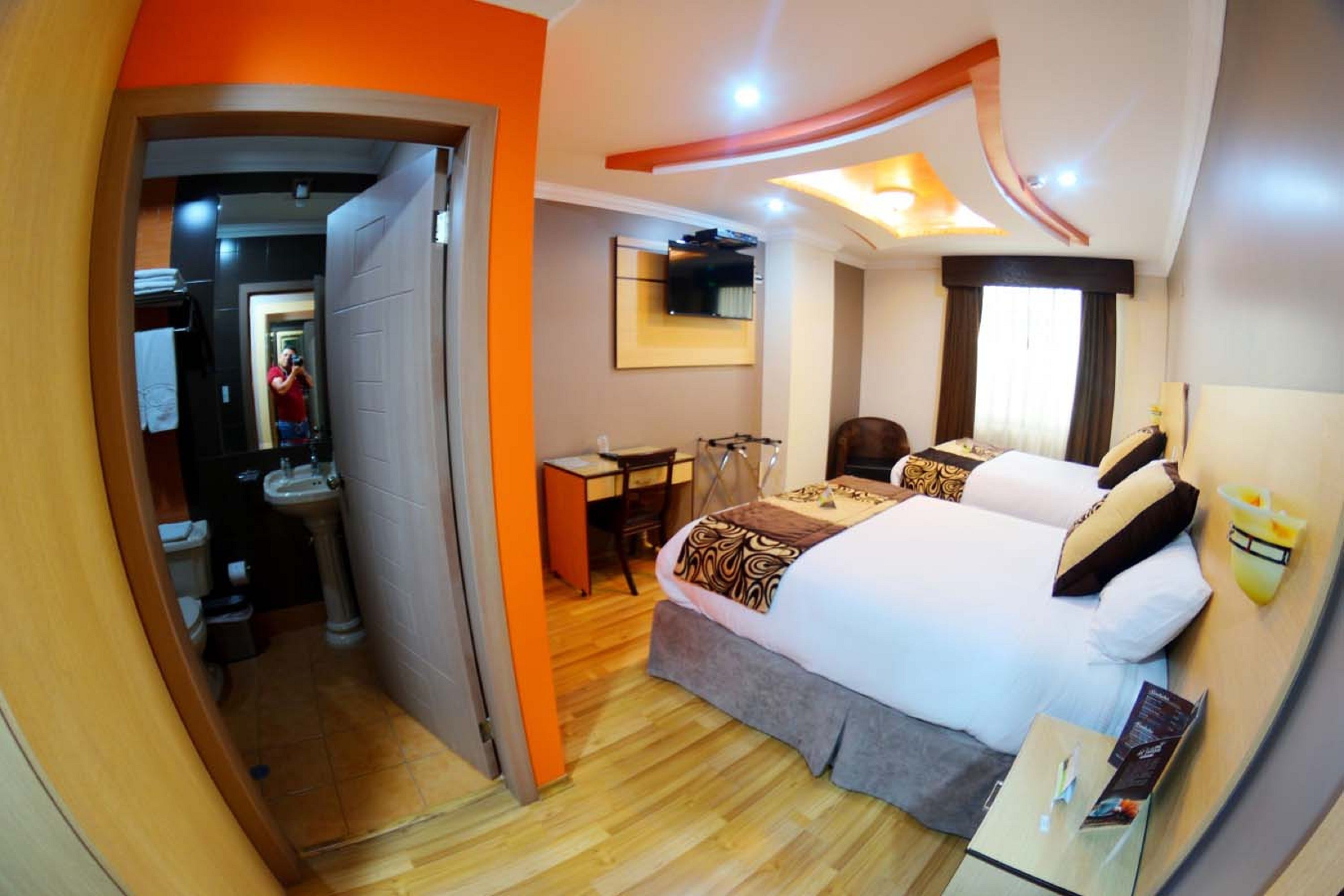A hotel room with a bed, bedside table, and a mirror.