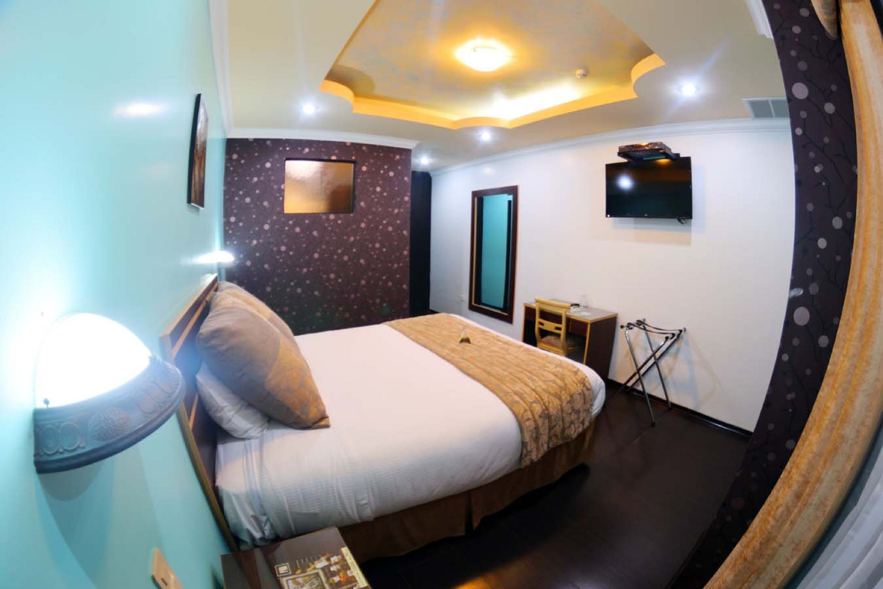 A hotel room with a bed, a flat-screen TV mounted on the wall, a small table, and a chair.
