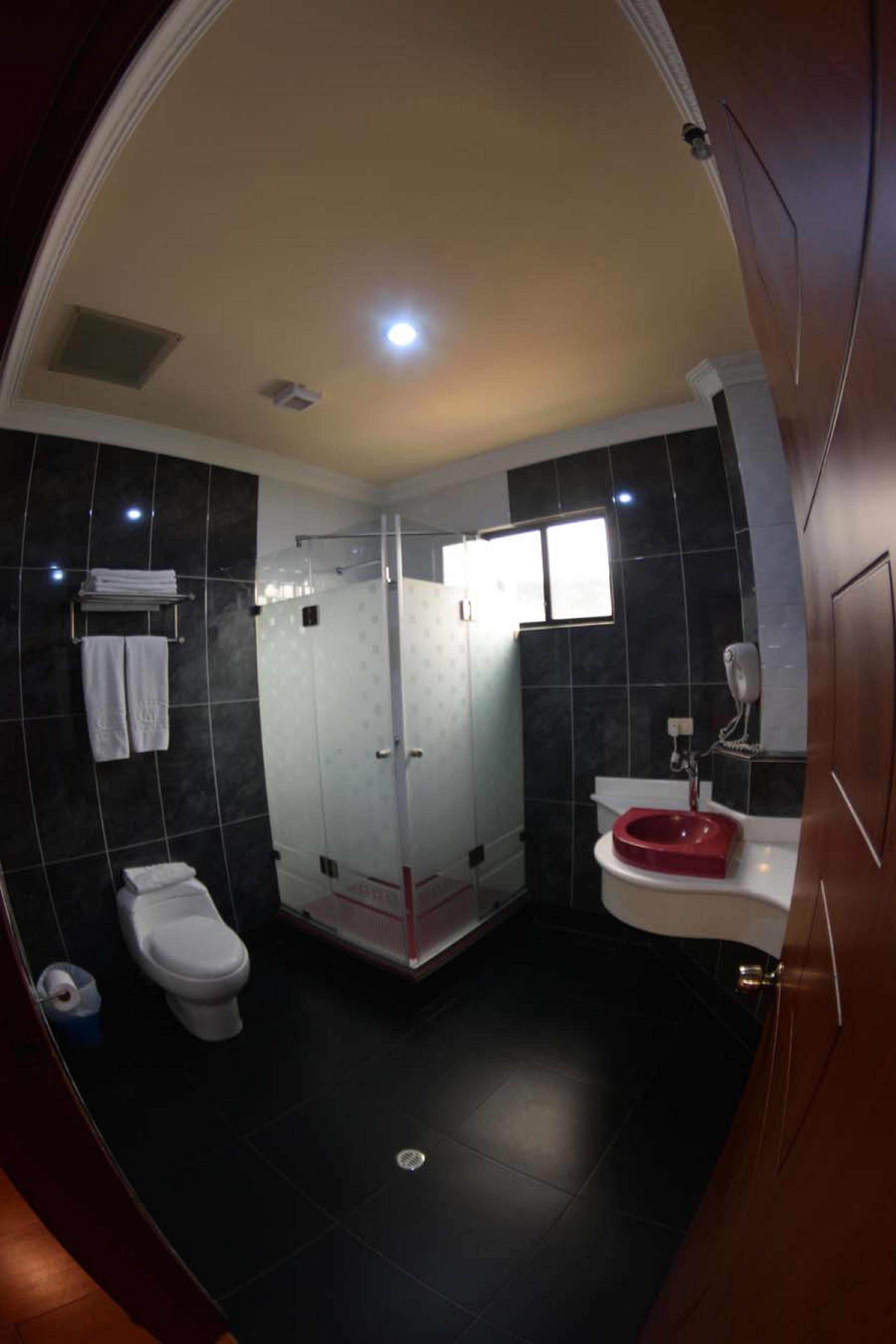 Un baño moderno con ducha de vidrio, inodoro blanco y lavamanos rojo.