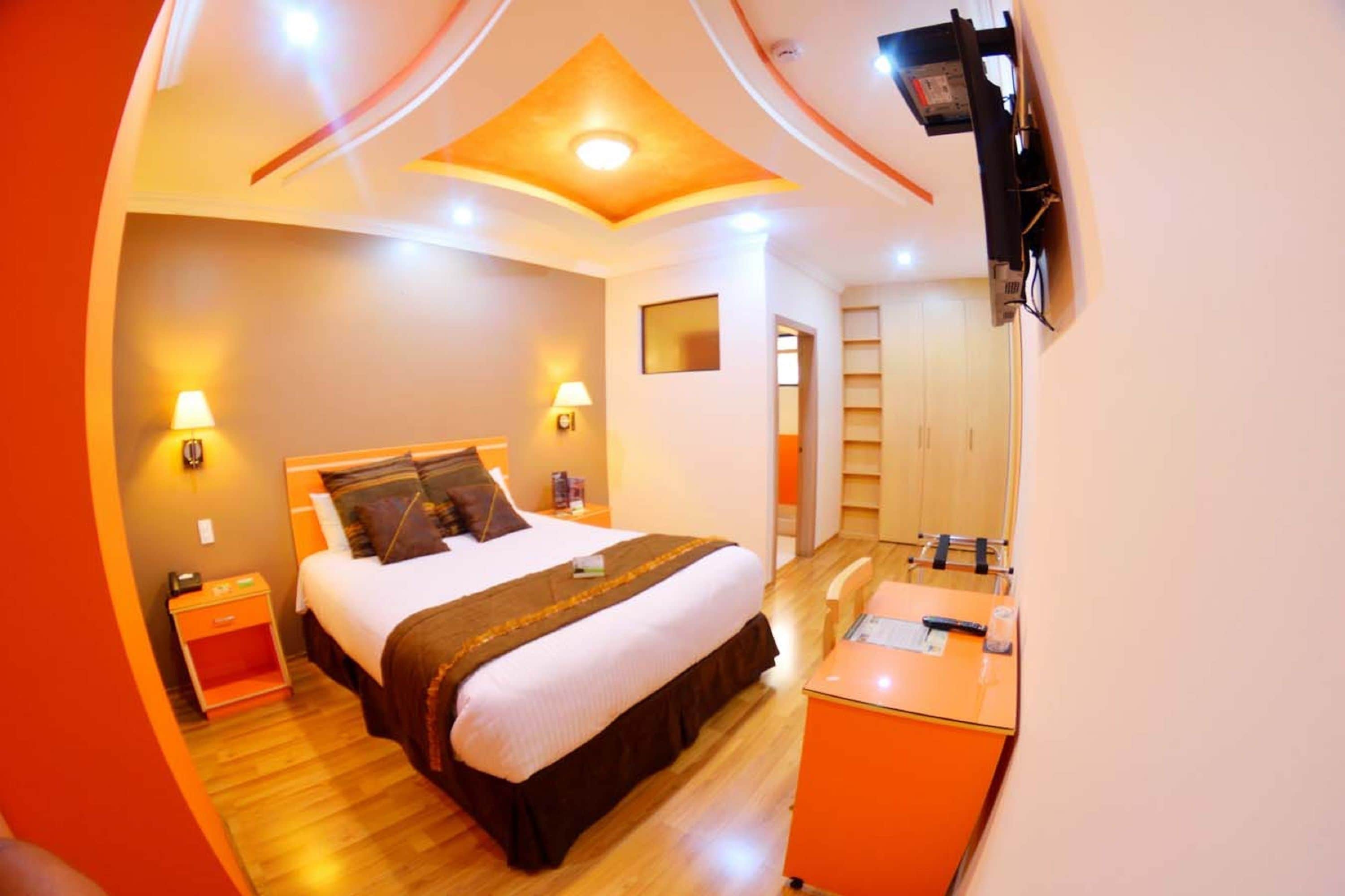 A hotel room with a bed, bedside table, lamp, and a desk with a chair.