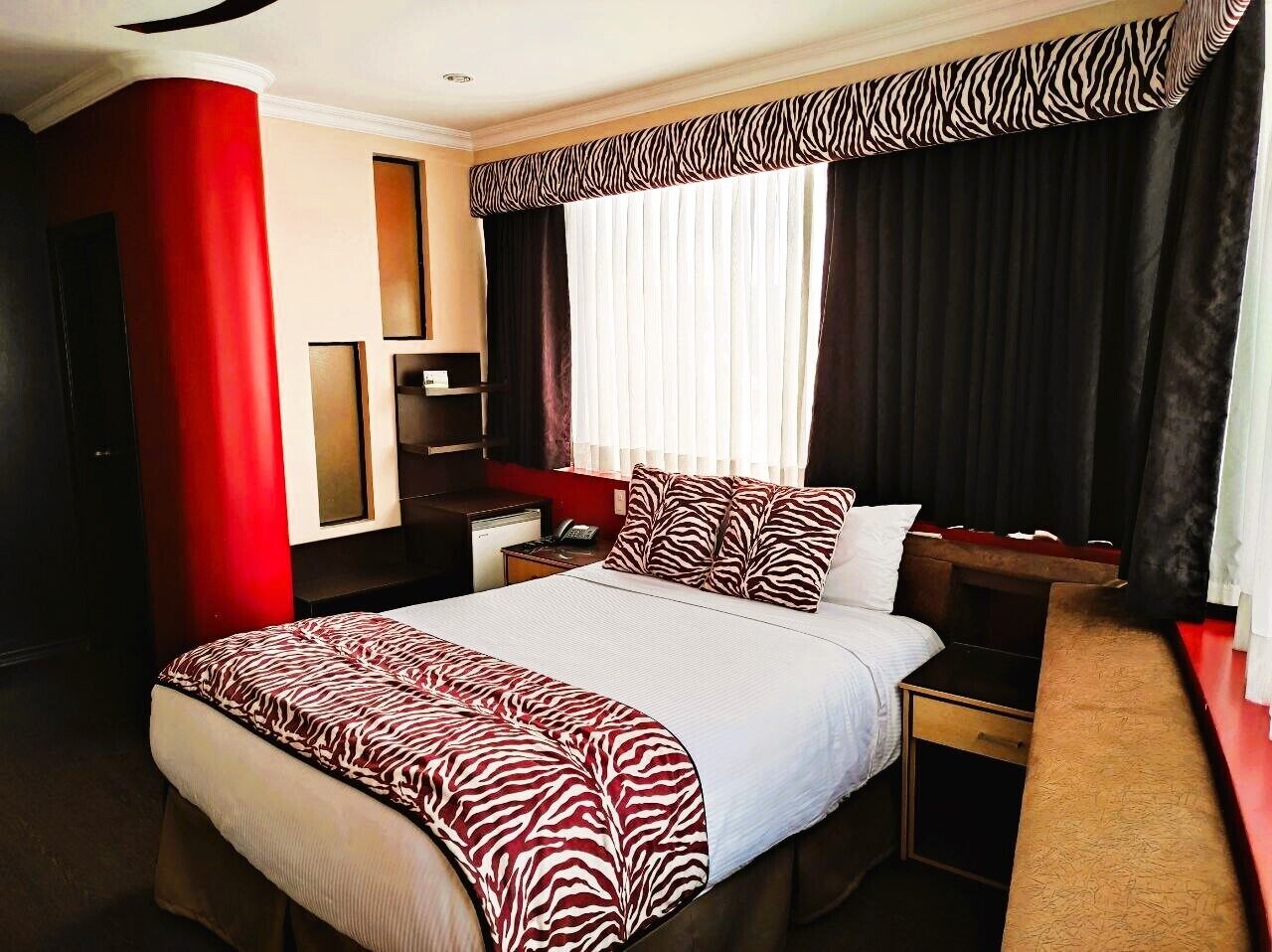 Habitación de hotel con una cama grande, un escritorio, una silla, un armario y un espejo.