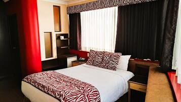 Habitación de hotel con una cama grande, un escritorio, una silla, un armario y un espejo.
