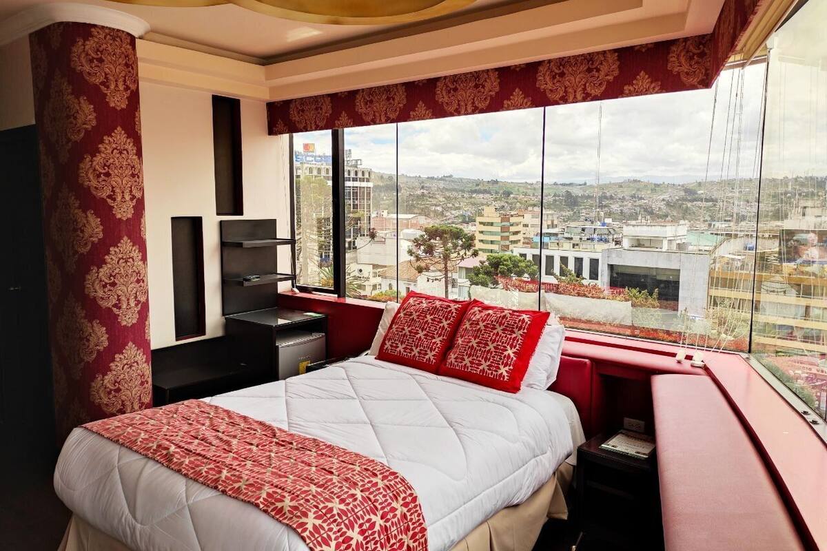 A hotel room with a large bed, a desk, and a view of the cityscape.