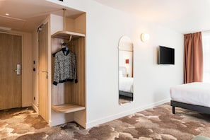 A hotel room with a bed, a mirror, a TV, a wardrobe, and a carpeted floor.