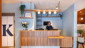 Un mostrador de recepción con detalles de madera, un gran letrero con la letra 'K' y una planta en la barra.