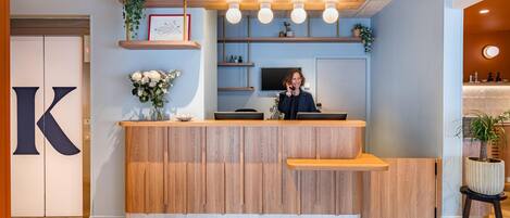 A reception desk with a wooden finish, a large 'K' sign, and a plant on the counter.