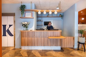 A reception desk with a wooden finish, a large 'K' sign, and a plant on the counter.