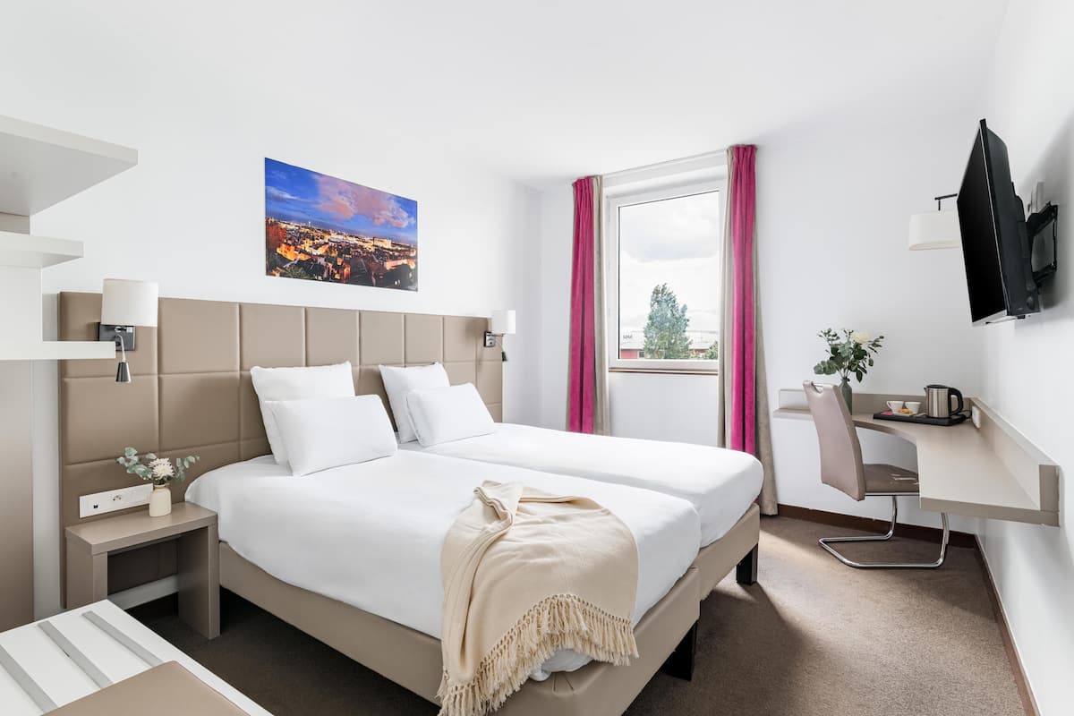Une chambre d’hôtel moderne équipée d’un lit, d’une table de chevet, d’un bureau, d’une chaise et d’un téléviseur fixé au mur.