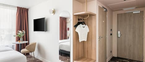 A hotel room with a bed, a TV, a mirror, a small table with a vase, and a wardrobe.