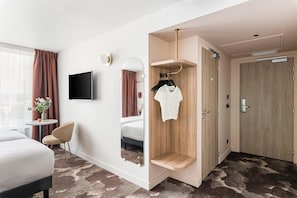 Habitación de hotel con cama, televisión, espejo, una mesita con un florero y un armario.