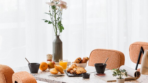 Una mesa de desayuno con pasteles, un florero y un libro.