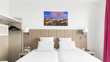 A hotel room with two beds, a cityscape view, a headboard, bedside lamps, a nightstand, and a hanging coat rack.