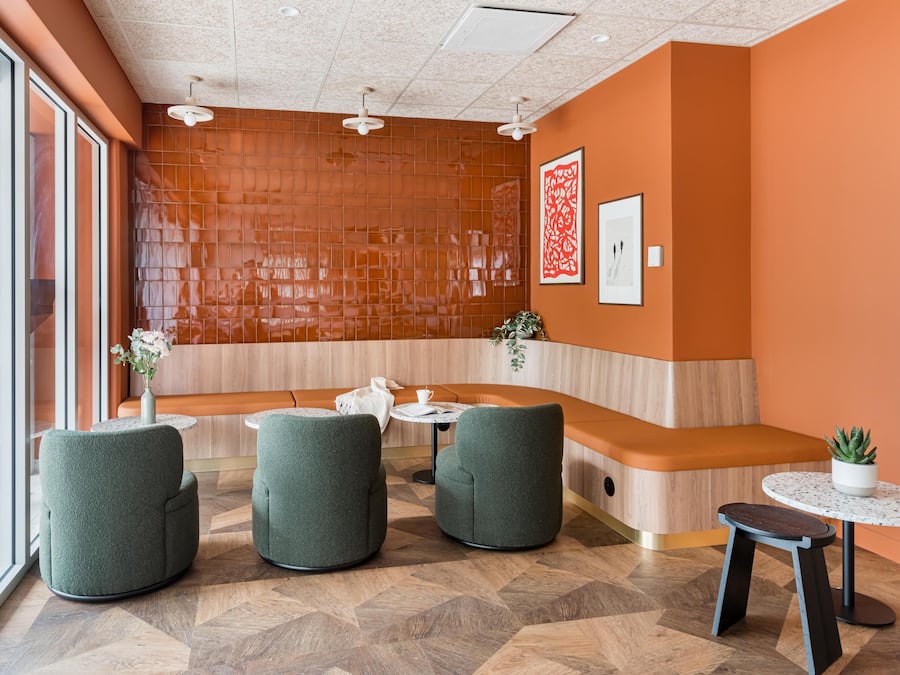 A reception area with a wooden panel wall, green upholstered seating, a small table with a plant, and a framed picture on the wall.