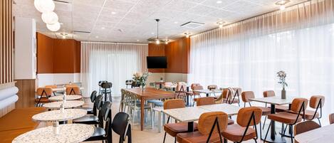 A hotel lobby with round tables, chairs, a TV, and large windows.