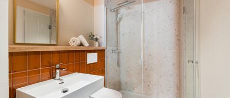 A bathroom with a white sink, a toilet, a glass shower enclosure, and a mirror with a gold frame.
