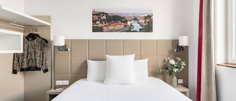 A hotel room with a bed, a cityscape view, a red curtain, and a vase with flowers.